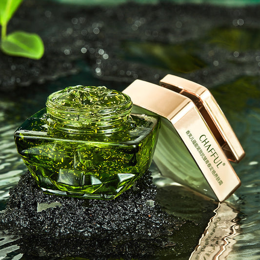 Green cosmetic jar with rose gold lid on a reflective surface with blurred green leaves in the background