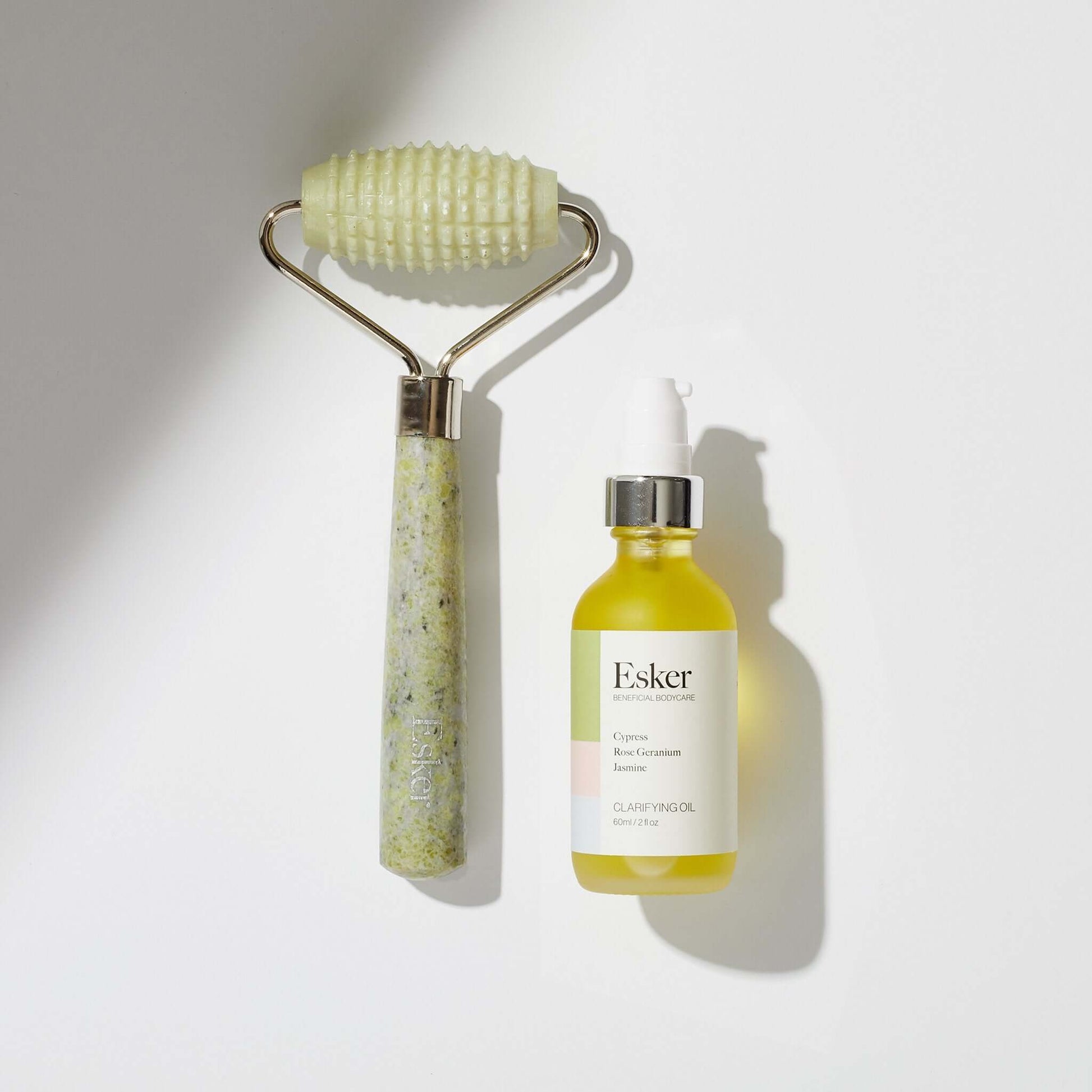 Jade skincare roller and bottle of oil with 'Esker' branding on a white background