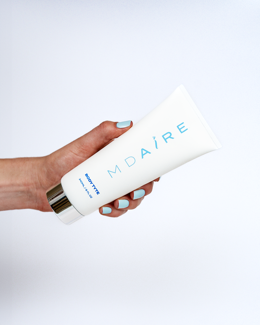 Hand with light blue-painted nails holding a white MDAiRE product against a light gray background